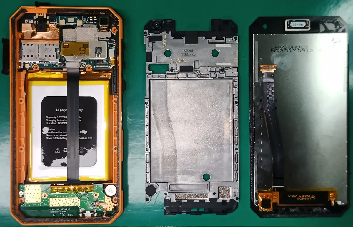 Celular real desmontado: placa, bateria e tela separadas sobre uma mesa