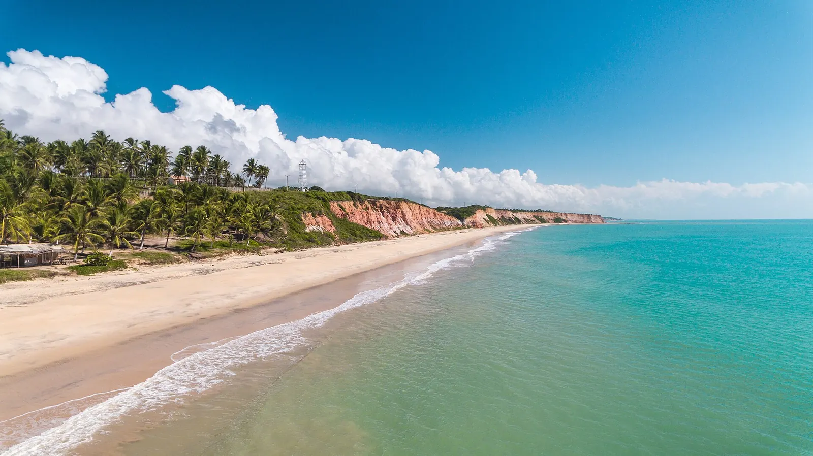 Praia de areia clara e mar verde-azulado em Prado, com falésias ao fundo